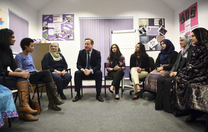 David Cameron speaks with women attending an English language class / Reuters