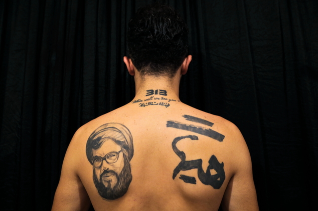 In this Tuesday, July 19, 2016 photo, Hamza, 25, poses for a photo showing off his tattoos of Hezbollah leader Hassan Nasrallah and Shiite Muslim religious slogans in the southern suburb of Beirut, Lebanon. The tattoo in Arabic reads, "It is impossible to humiliate us." A growing number of Shiite Muslims in Lebanon are getting tattoos with religious and other Shiite symbols since the civil war in neighboring Syria broke out five years ago, fanning sectarian flames across the region. (AP Photo/Hassan Ammar)